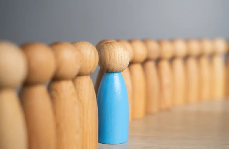 Rangée de quilles en bois avec une figurine bleue qui se distingue — la transformation au-delà de la simple conformité.