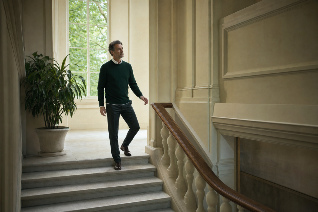 Un homme descend un large escalier de pierre, vu de trois-quarts, le visage tourné vers la lumière d'une haute fenêtre, un pied encore sur la marche du dessus.
