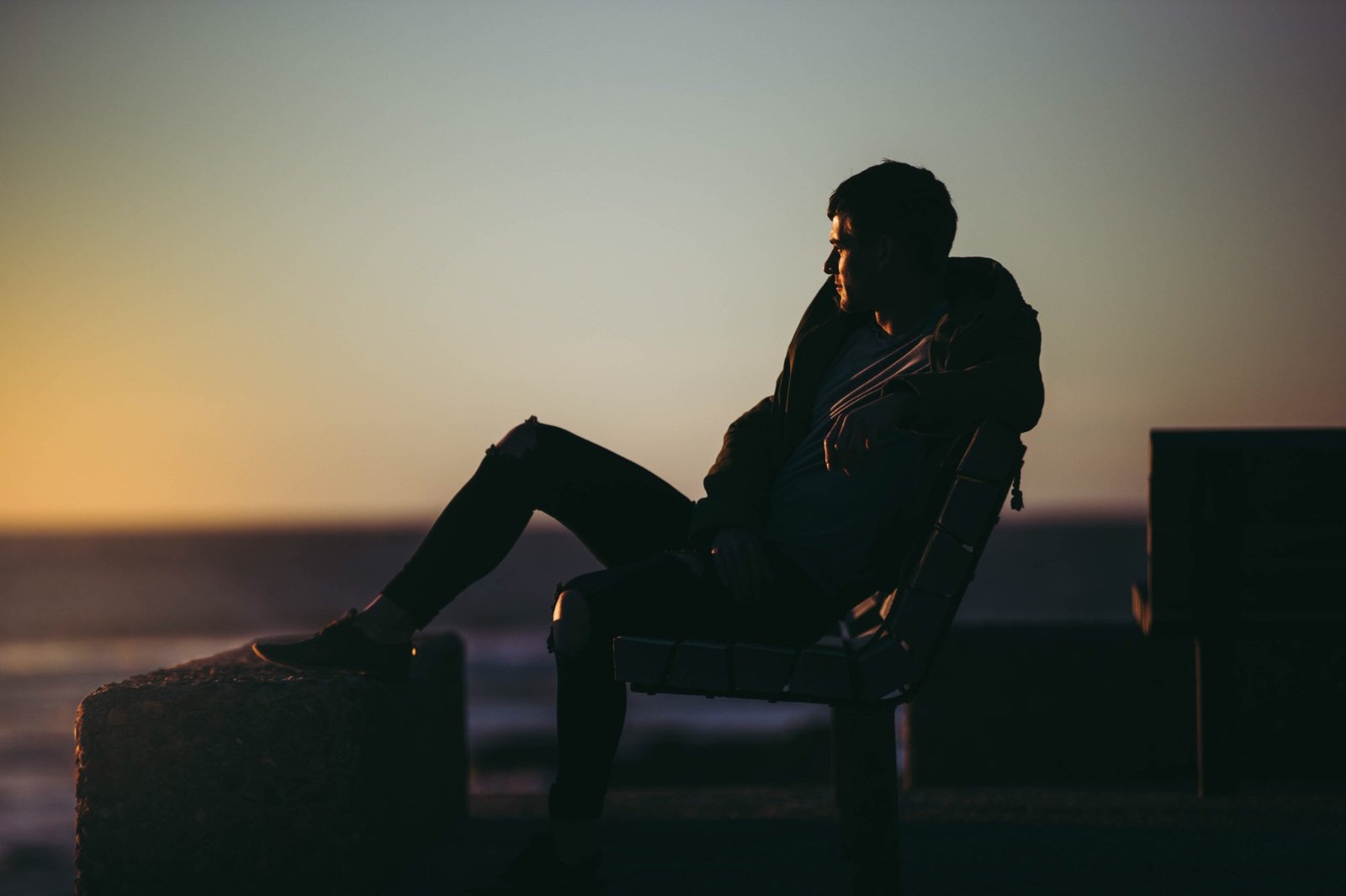 Un homme assis au repos face à la mer, au coucher du soleil