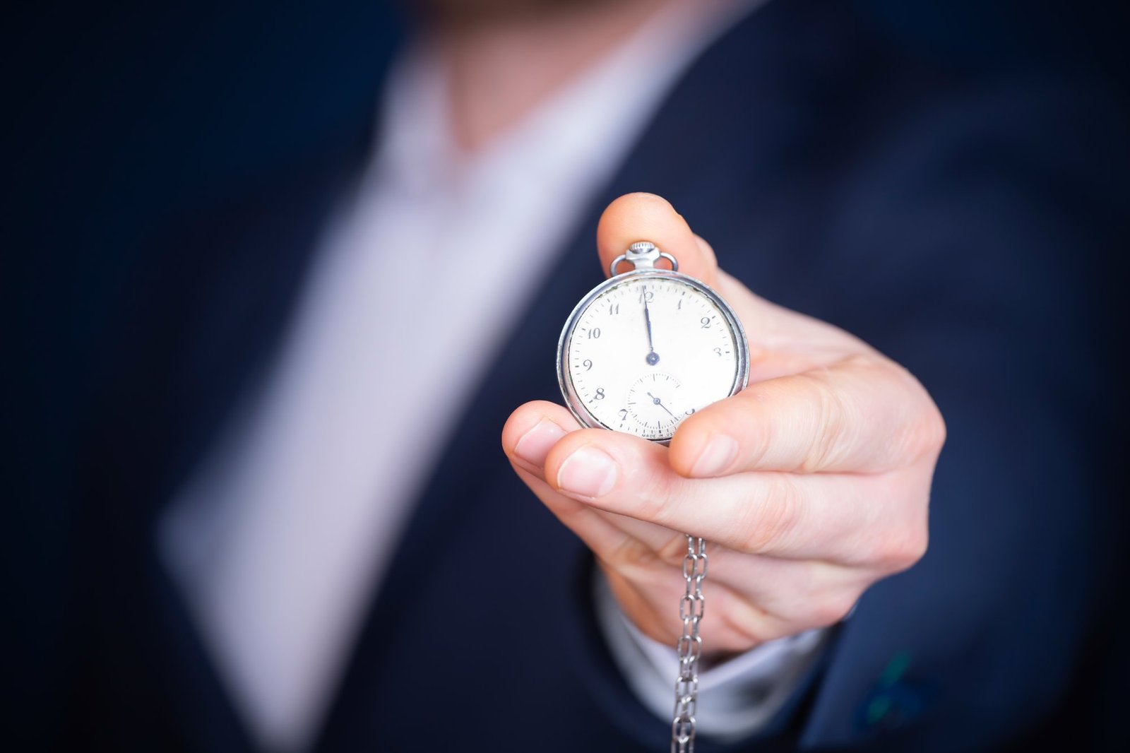 Une main tenant une montre à gousset devant un costume bleu nuit